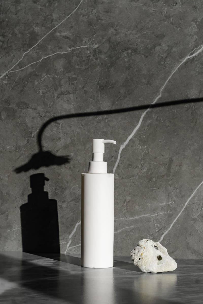 A plain white pump bottle casting a soft shadow on pale marble