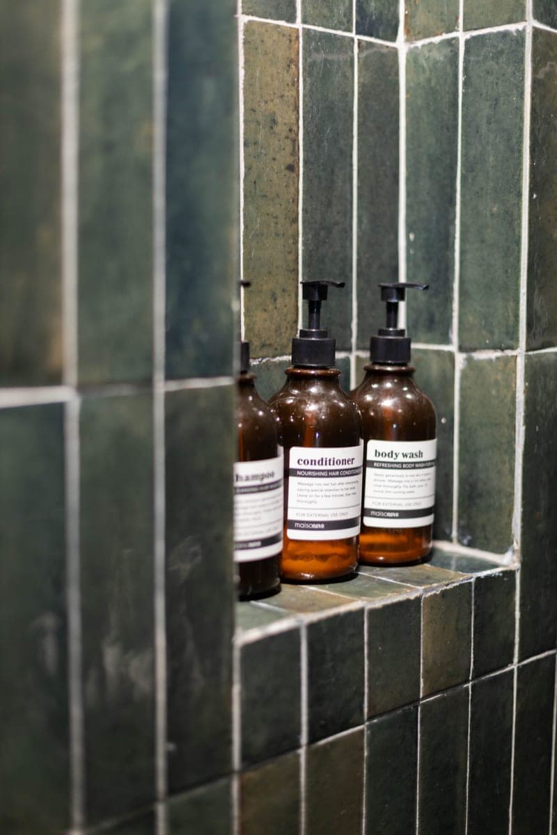 Amber bottles of shampoo, conditioner and body wash in a tiled shower