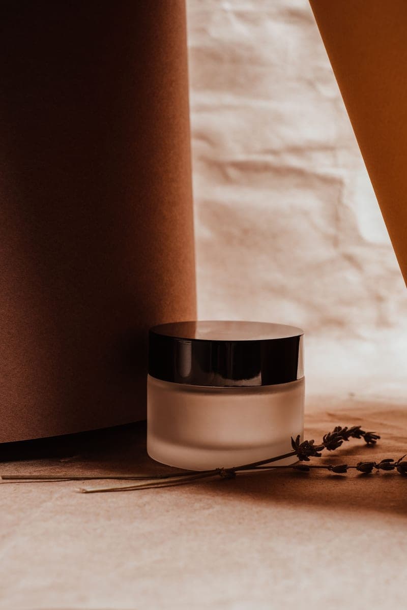 A small glass jar beside dried lavender in warm brown tones
