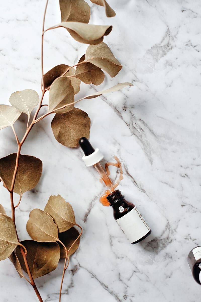 A serum bottle and a eucalyptus sprig laid flat on a marble surface