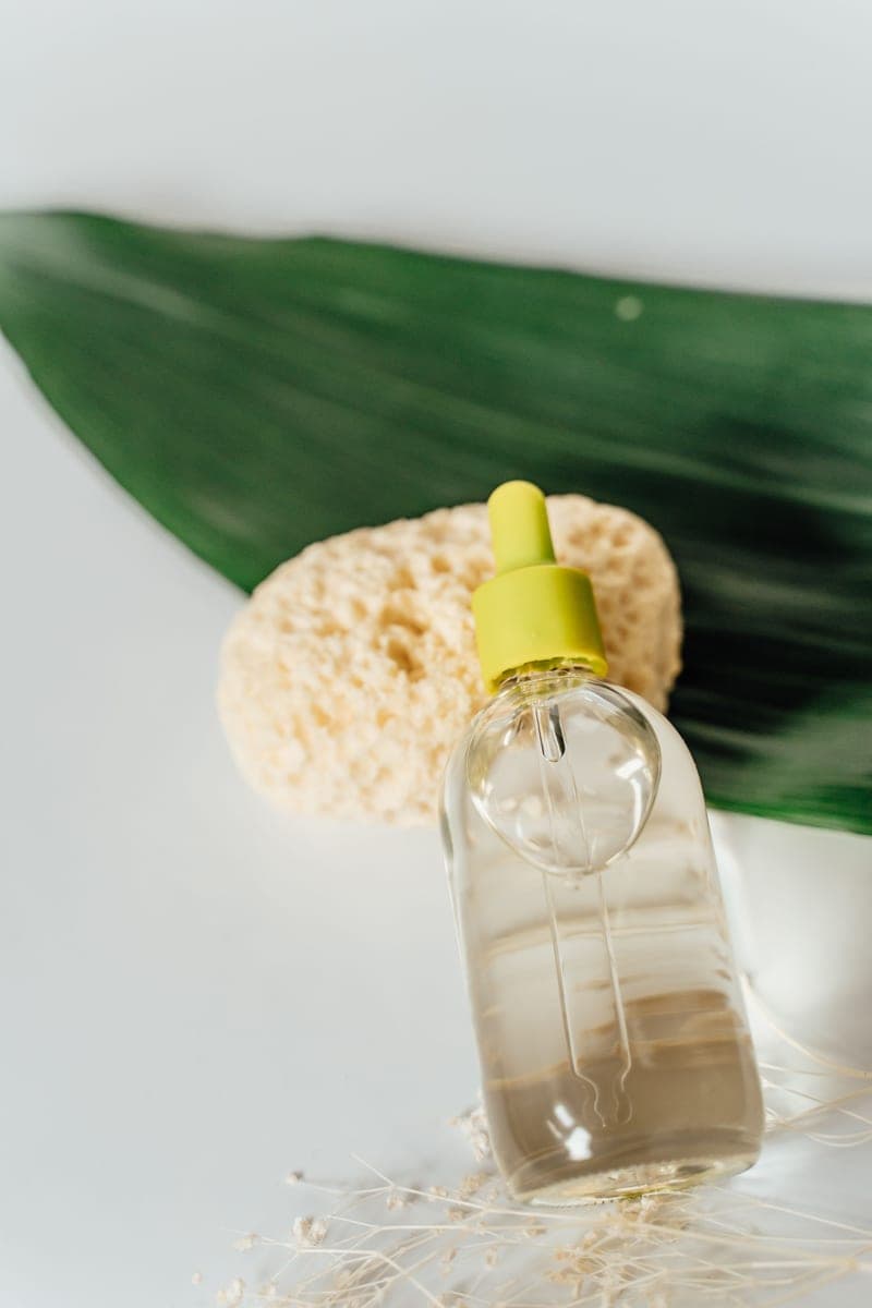 A cosmetic oil bottle beside a green leaf