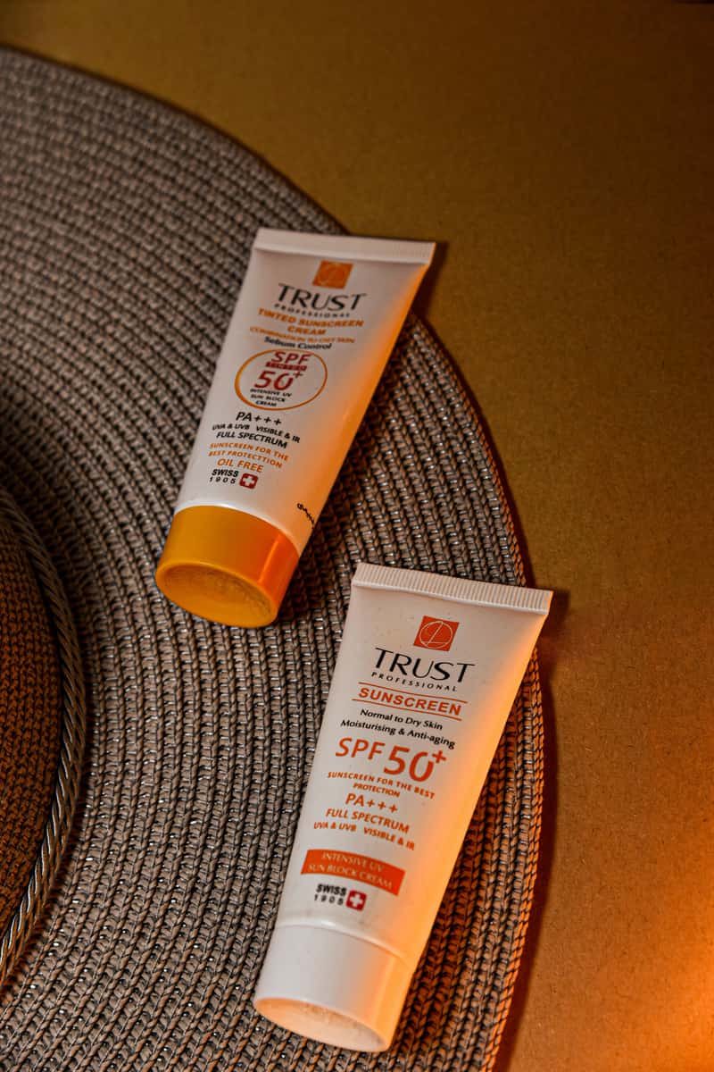 Two SPF 50 sunscreen tubes on a woven mat in warm light