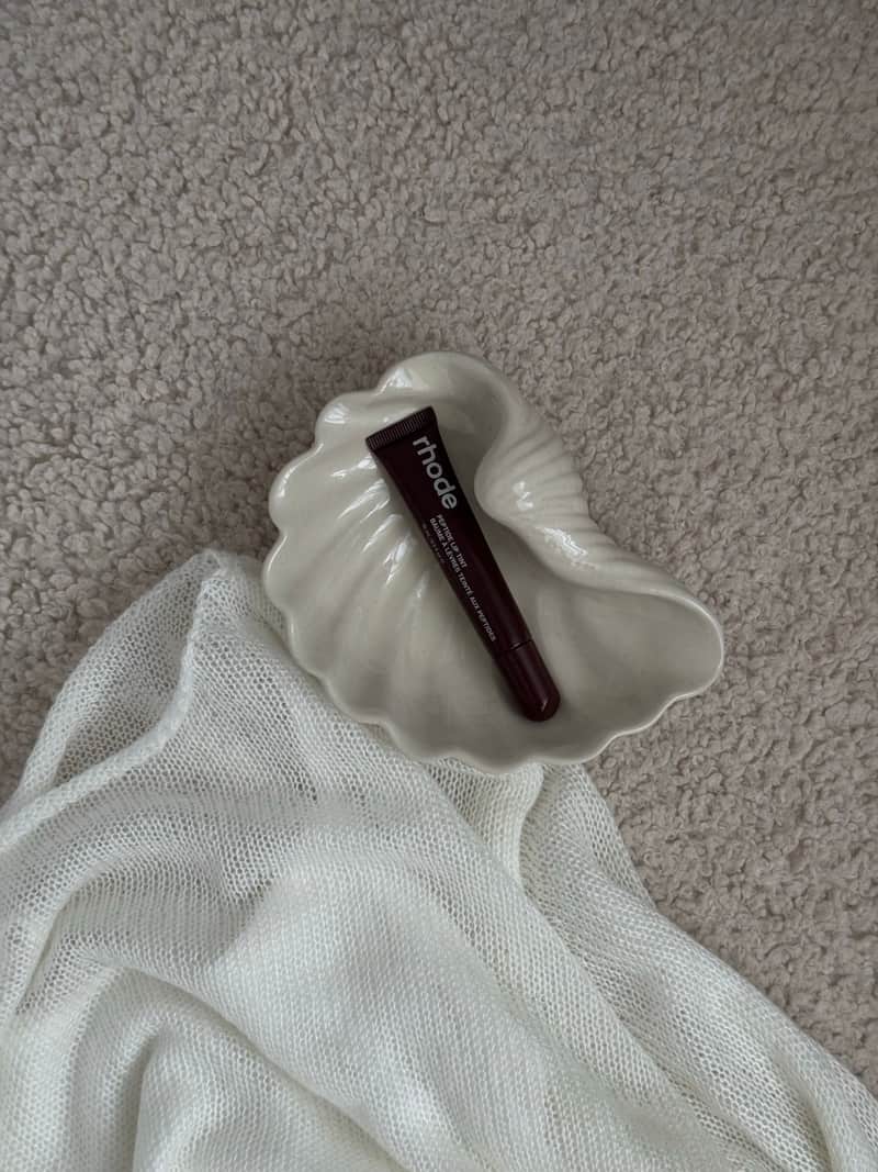 A skincare tube resting in a ceramic shell dish on textured fabric