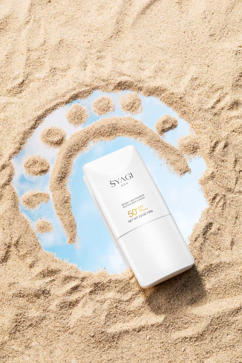 An SPF 50 sunscreen bottle standing on sand