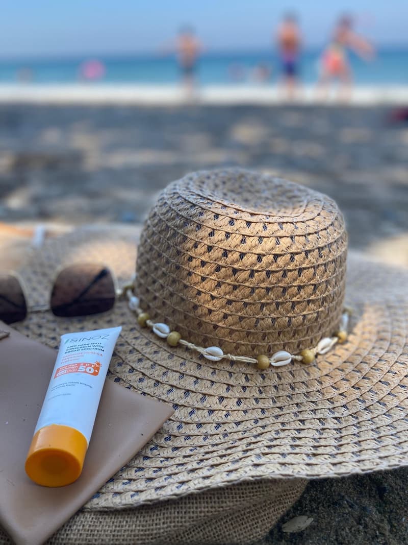 A straw hat and a sunscreen bottle on a sandy beach